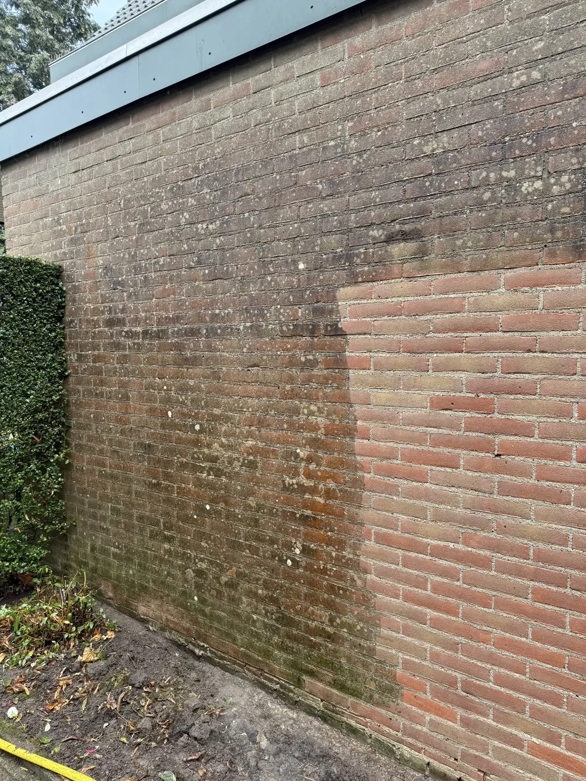 Half gereinigde bakstenen muur: links nog vervuild, rechts weer warm rood